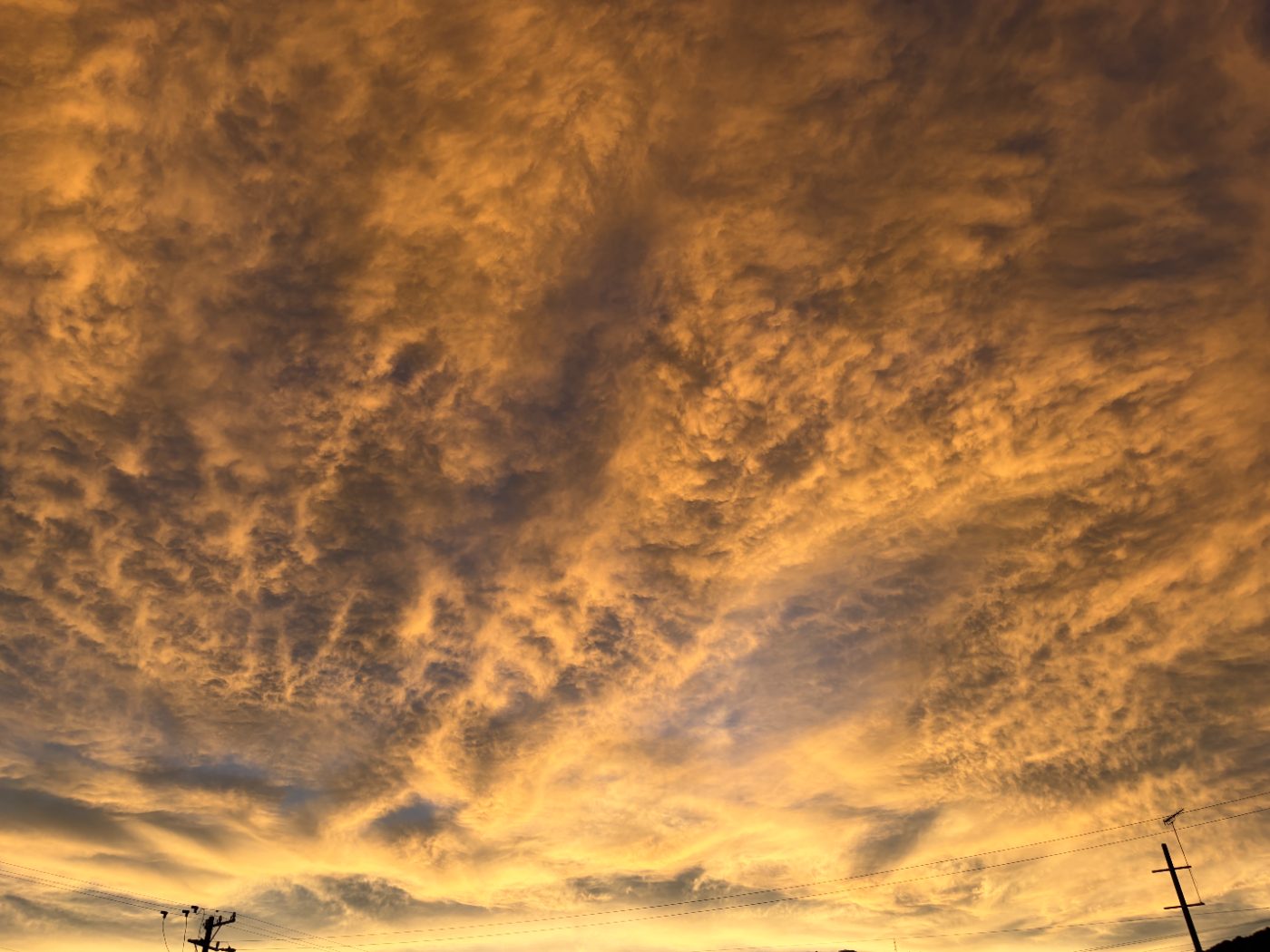 山の稜線と電柱のシルエットの上に広がる、黄金色に染まった夕方の雲