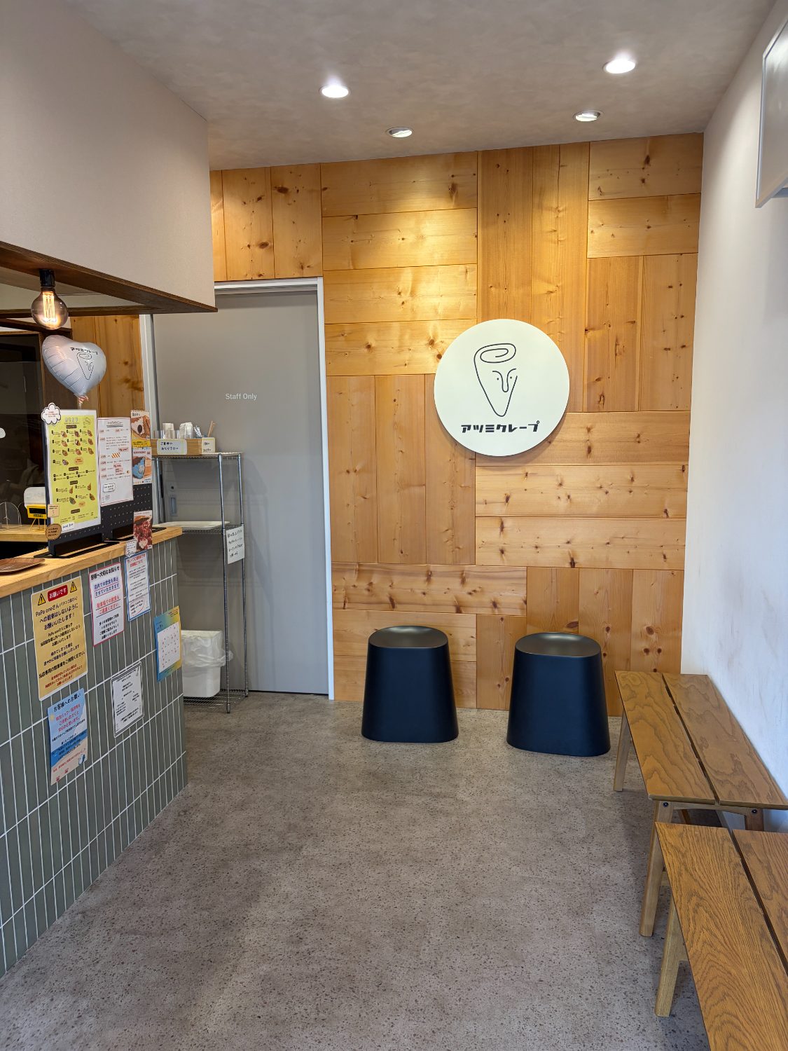 アツミクレープの店内。木の壁とロゴの丸看板、待合用のベンチ