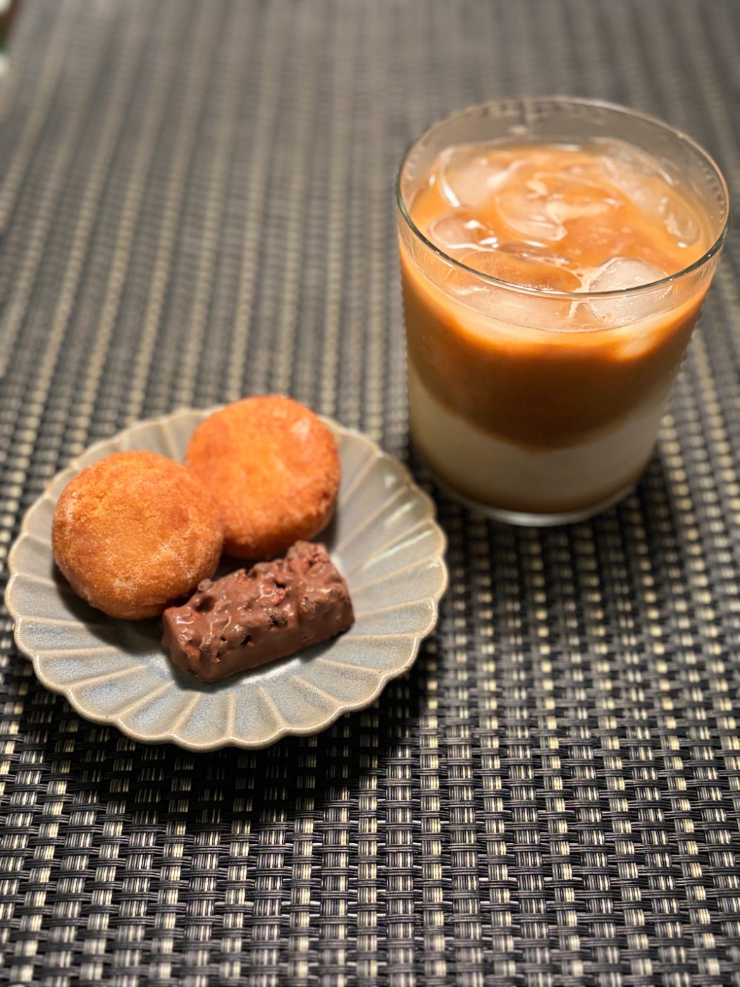 二層になったアイスカフェラテと、皿にのせた二つのドーナツとチョコレート菓子