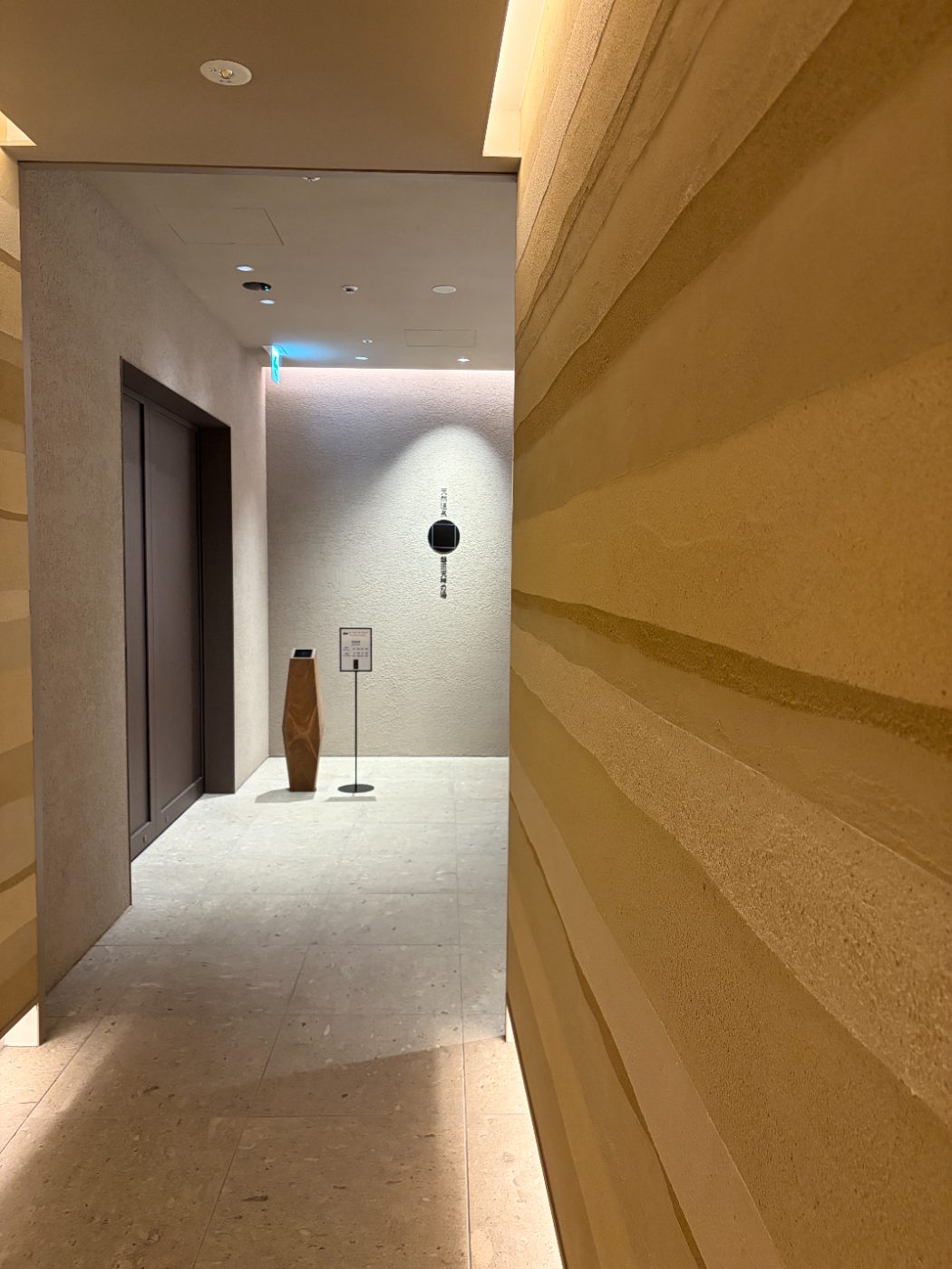 版築の壁が続く館内の通路。奥に浴場の入口の看板が見える