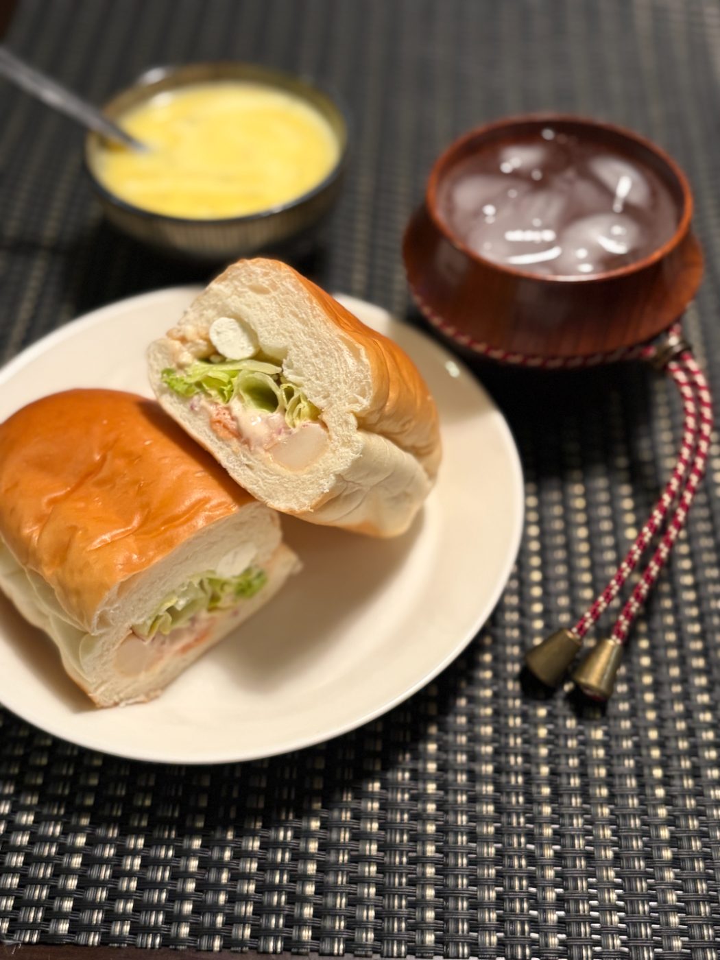 半分に切ったスモークサーモンクリームチーズのコッペパン。奥にスープと木のカップ