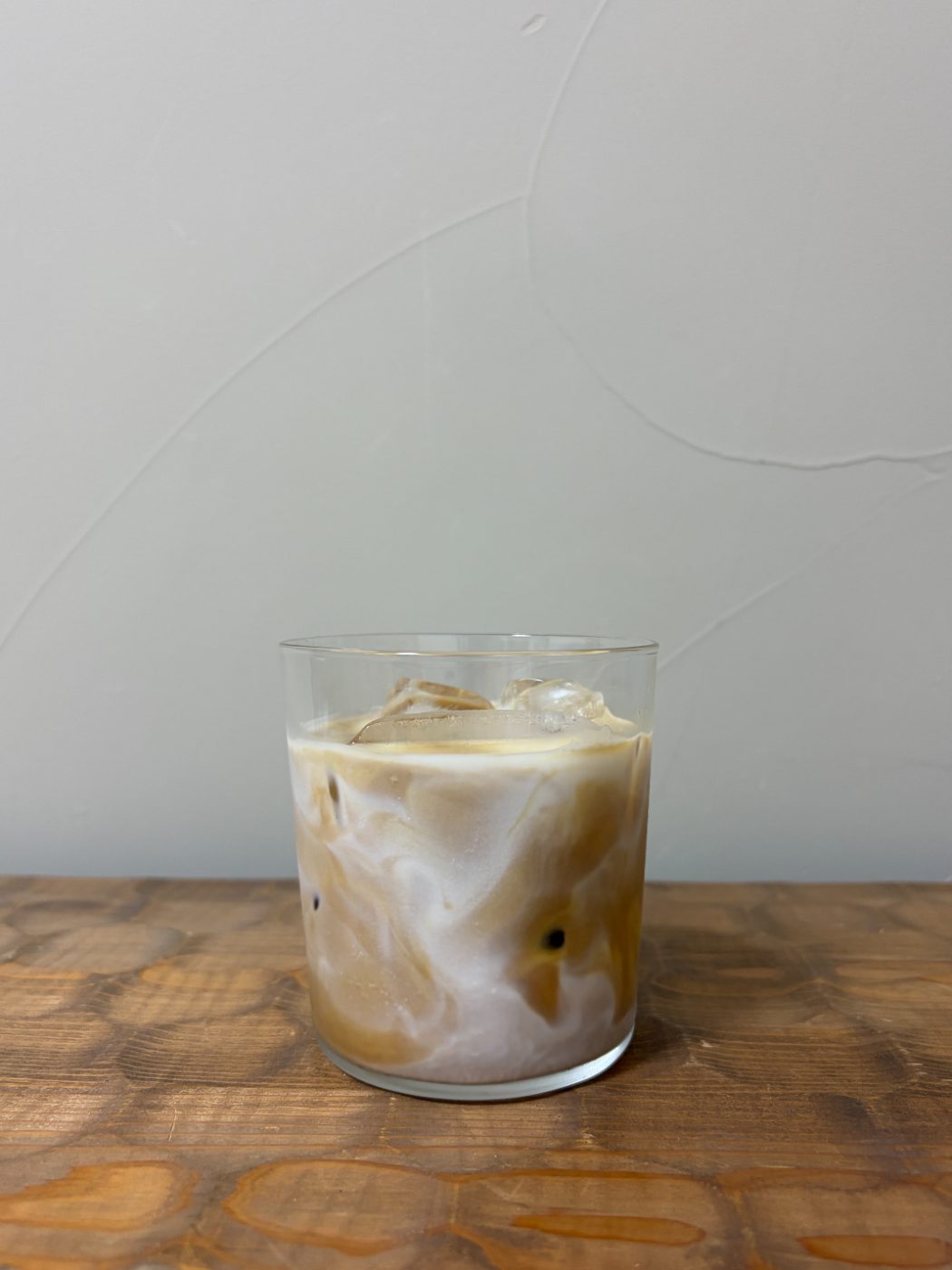 木のテーブルに置かれたアイスカフェラテ。ミルクとコーヒーがまだ混ざりきっていない