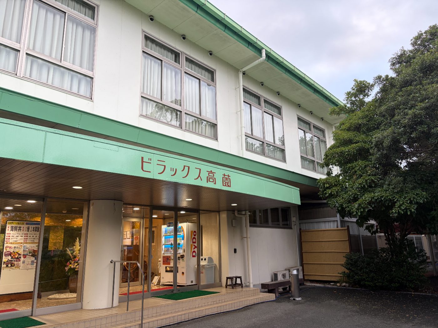 ホテル ビラックス高薗の外観。緑の庇と自動ドア、掲示されたメニュー